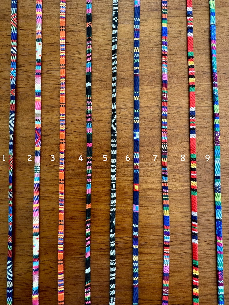 May include: Nine colorful woven cords, numbered 1 through 9, are displayed against a woodgrain background. Each cord features a unique pattern of stripes and colors.
