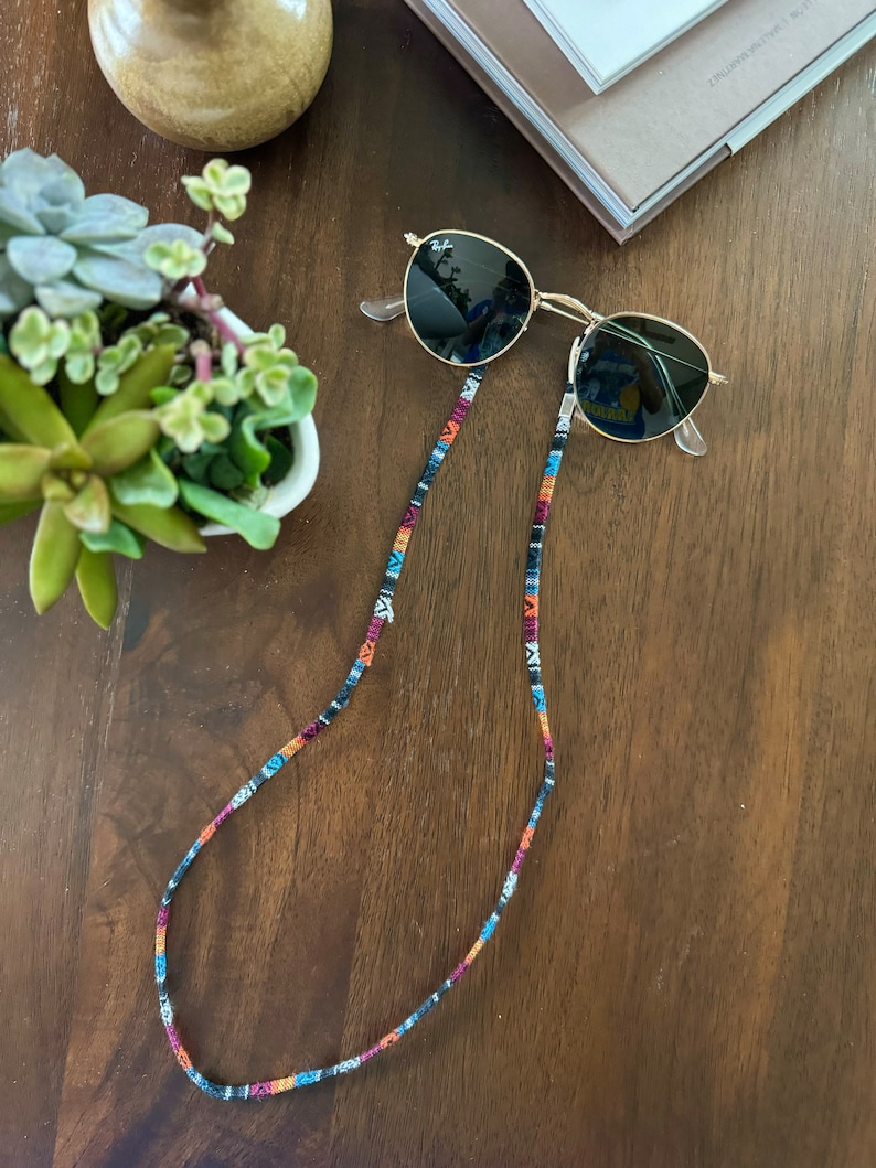 May include: A pair of round, black sunglasses with a gold frame and a colorful, patterned eyeglass chain.