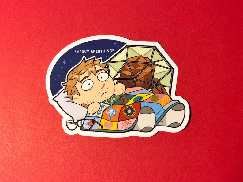 K&ouml;nnte beinhalten: Ein Aufkleber mit einer Zeichentrickfigur mit hellbraunem Haar, die unter einer bunten Patchwork-Decke liegt. Die Figur hat weit aufgerissene Augen und dar&uuml;ber steht der Text *HEAVY BREATHING*. Hinter der Figur befindet sich eine geometrische Kuppelstruktur.