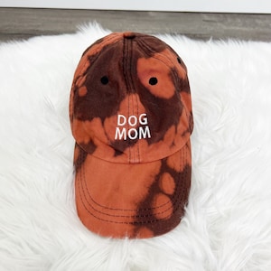 May include: A brown and orange tie-dye baseball cap with the text "DOG MOM" embroidered in white.