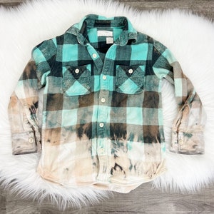 Puede incluir: Una camisa de franela a cuadros de color turquesa y marrón con un efecto blanqueado. La camisa tiene un frente abotonado y mangas largas.