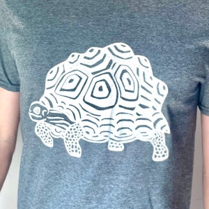 May include: A gray t-shirt with a white graphic of a stylized turtle with a patterned shell.