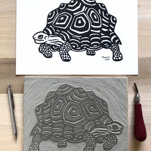 May include: A black and white linocut print of a tortoise with a detailed shell pattern. The print is on a white background and is signed and dated "S. Sanchez 2020".