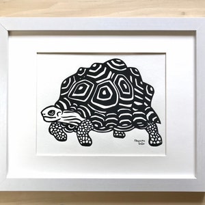 May include: Black and white illustration of a turtle with a patterned shell in a white frame.