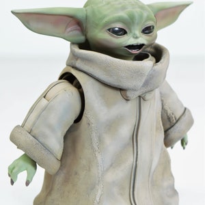 May include: An articulated action figure of a fictional character from the Star Wars franchise. The figure is green and brown, wearing a brown coat with a fur collar and has large ears.