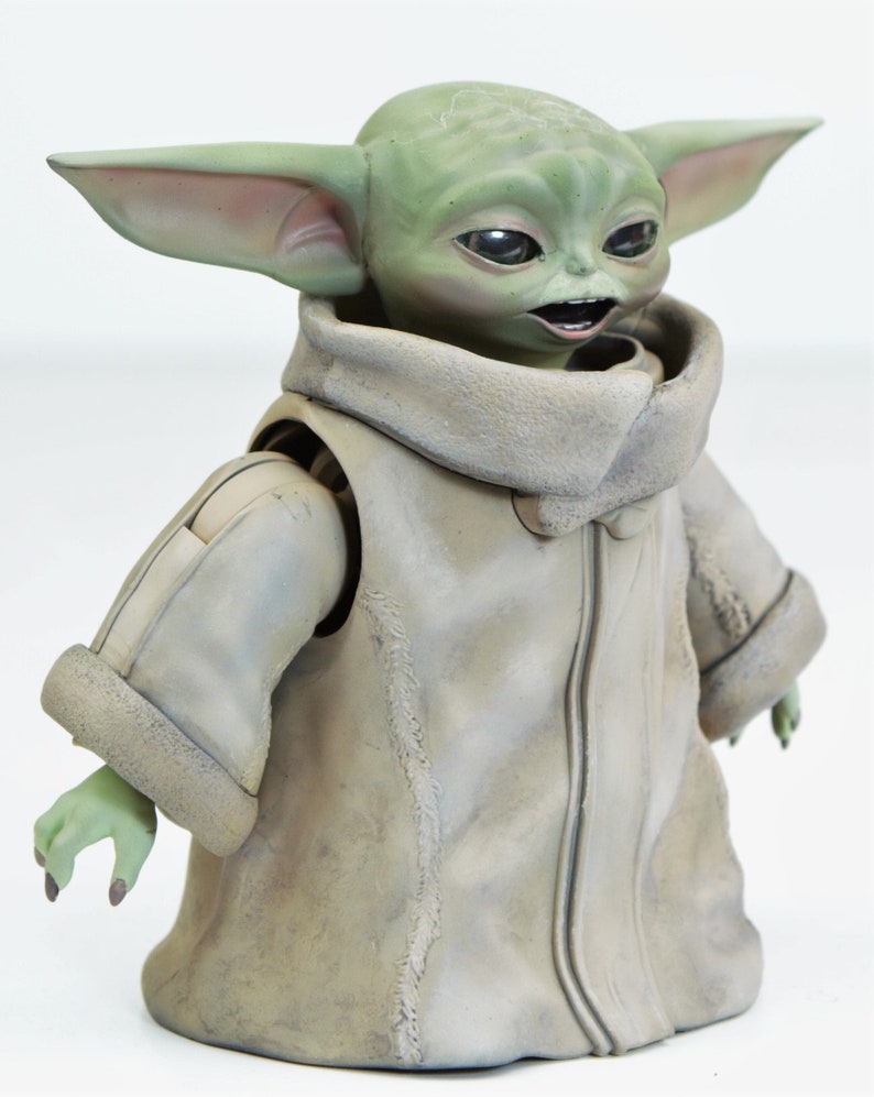May include: An articulated action figure of a fictional character from the Star Wars franchise. The figure is green and brown, wearing a brown coat with a fur collar and has large ears.