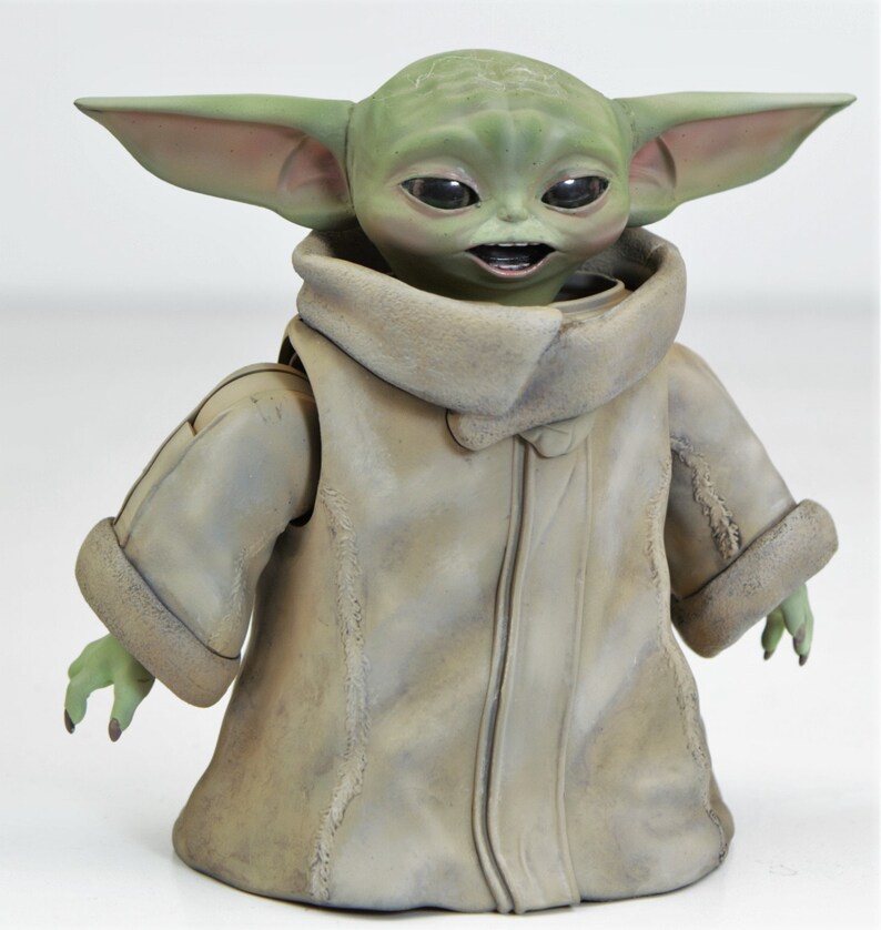 May include: A green and brown plush toy of a character from the Star Wars franchise. The toy is wearing a brown coat with a fur collar and has large ears.