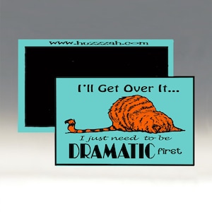 May include: A turquoise blue square magnet featuring a cartoon orange cat curled up. The text "I'll Get Over It... I just need to be DRAMATIC first" is printed on the magnet.