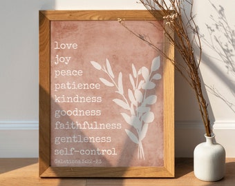 Può includere: Una stampa incorniciata con sfondo rosa e testo bianco. Il testo recita "love, joy, peace, patience, kindness, goodness, faithfulness, gentleness, self-control, Galations 5:22-23". Un motivo floreale bianco si trova sul lato destro della stampa.