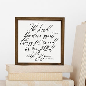 May include: A framed wood sign with a white background and black calligraphy text that reads "The Lord has done great things for us and we are filled with joy" with the scripture reference "PSALM 126:3" at the bottom.