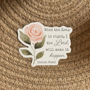 May include: A white sticker with a watercolor illustration of a pink rose. The sticker has a quote from the Bible, Isaiah 60:22, which reads "When the time is right, I the Lord, will make it happen."