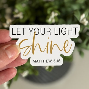 May include: White sticker with black text "Let your light shine" and gold text "shine" with the bible verse "Matthew 5:16" underneath.