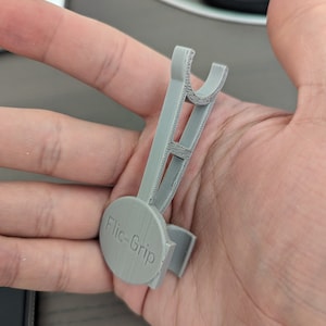 May include: A gray 3D printed phone grip with the text "Flic-Grip" printed on the front.