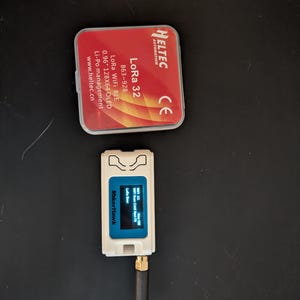 May include: A white MakerHawk device with a small blue screen and a black antenna, next to a red Heltec Automation case. The case has the text "LoRa 32" and other technical specifications.