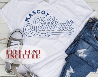 Pode incluir: Camiseta branca com um design azul que diz "MASCOT Softball" em uma fonte cursiva. O texto "FREE FONT INCLUDED" também está incluído em vermelho. A camiseta está sobre uma superfície de madeira com um par de tênis cinza e uma calça jeans azul.