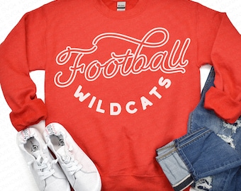 Pode incluir: Camisola vermelha com texto branco que diz "Football Wildcats" em uma fonte cursiva.