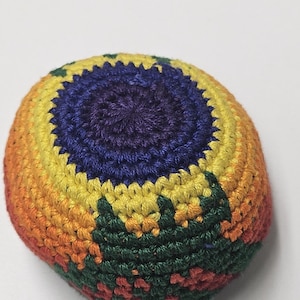 May include: A colorful, handmade crochet ball. The ball features a vibrant spectrum of colors, including orange, yellow, green, and blue. The crochet stitches are clearly visible, giving the ball a textured appearance. The ball is round and appears to be filled with a soft material.
