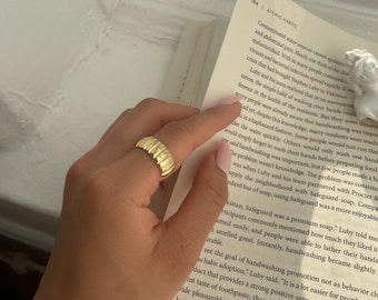 Könnte beinhalten: Nahaufnahme einer Hand, die einen goldenen Ring mit strukturiertem Design trägt. Die Hand hält ein Buch offen auf einer Seite mit Text über Händewaschen.