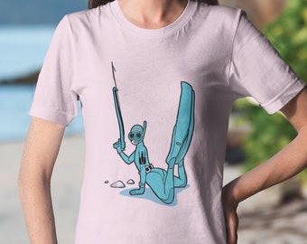 Könnte beinhalten: Ein pinkfarbenes T-Shirt mit einer Cartoon-Illustration einer Person, die eine Tauchermaske und Flossen trägt und eine Harpune hält. Die Person trägt einen blauen Tauchanzug und liegt mit dem Bauch auf dem Wasser.