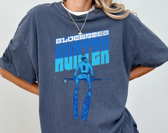 Puede incluir: Una camiseta azul oscuro con un gráfico vintage de un buceador con el texto "Bluewater Hunter" en azul y blanco.