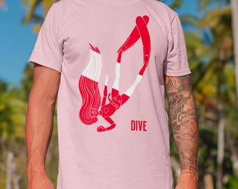 Könnte beinhalten: Ein hellrosa T-Shirt mit kurzen Ärmeln und einer rot-weißen Grafikillustration einer tauchenden Person. Die tauchende Person ist in einer abwärts schwimmenden Position mit langem Haar und Flossen dargestellt. Das Wort DIVE ist in Rot aufgedruckt.