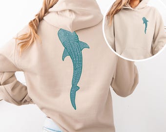 May include: A beige hoodie with a teal whale shark design on the back. The hoodie has a drawstring hood and a kangaroo pocket.