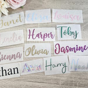 May include: A collection of name decals in various colors and fonts, including gold, pink, green, and glitter. Names include Janet, Eliza, Louisa, Amelia, Harper, Toby, Sienna, Olivia, Jasmine, Ethan, Ava, Harry, and Noah.