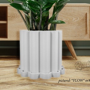May include: White ceramic planter with a fluted design and a scalloped edge. The planter is 8 inches in size and includes a drip tray. A green plant is growing in the planter.