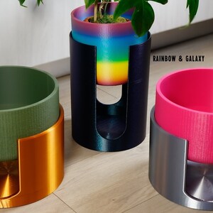 Può includere: Tre vasi per piante diversi con supporti abbinati. Il primo vaso è verde con un supporto in rame, il secondo vaso è rosa con un supporto in argento e il terzo vaso è arcobaleno con un supporto nero. Il testo "Rainbow & Galaxy", "Green & Copper" e "Pink & Silver" è stampato sotto ogni vaso.
