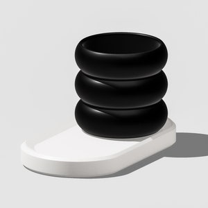 May include: A black ceramic planter with four stacked rings sits on a white oval base.