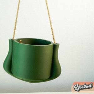 Può includere: Un vaso da fiori sospeso di colore verde scuro con un gancio in corda. Il vaso ha una forma arrotondata leggermente svasata.