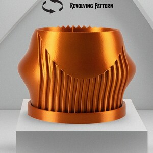 May include: A copper-colored, 3D printed, rotating planter with a ribbed design. The planter has a drip tray and a revolving pattern.