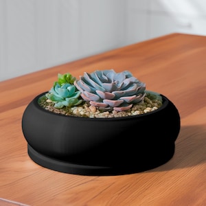 May include: A black ceramic planter with a rounded shape, filled with small succulents. The planter is sitting on a wooden surface.