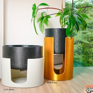 May include: Two plant stands, one white and one gold, with black plant pots. The gold stand has a plant with green leaves. The text "Black & Gold" is printed below the gold stand. The text "Black & White" is printed below the white stand.
