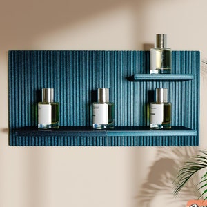 May include: Four glass bottles with silver caps and clear liquid sit on a teal blue shelf with black trim. The shelf is mounted on a wall with a textured teal blue surface.