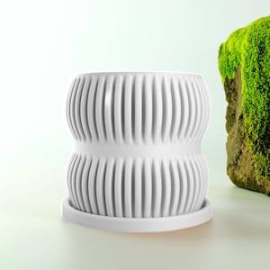 Peut inclure: Pot en céramique blanche avec un design côtelé. Le pot a deux sections, créant une forme arrondie. Le pot est posé sur une surface blanche.