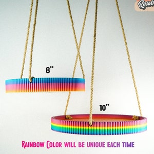 May include: Two rainbow colored hanging trays with rope. The top tray is 8 inches in diameter and the bottom tray is 10 inches in diameter. "Rainbow Color Will Be Unique Each Time" is written below the trays.