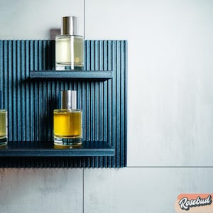 Könnte beinhalten: Drei Glasflaschen mit Parfüm auf einem dunkelblauen Regal mit vertikalen Linien. Die Flaschen sind aus klarem Glas mit silbernen Kappen. Das Parfüm in den Flaschen ist gelb und klar.