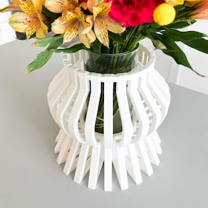 May include: White vase with a geometric design, holding a bouquet of pink carnations and yellow alstroemeria flowers.