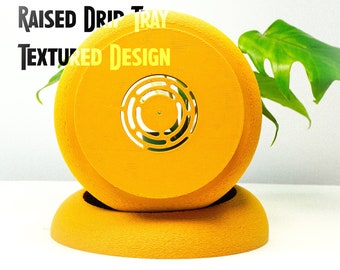 May include: A yellow, textured, raised drip tray with a circular cutout in the center. The text "OPTIMAL DRAINAGE RAISED DRIP TRAY TEXTURED DESIGN" is printed on the tray. The tray is sitting on a white surface.
