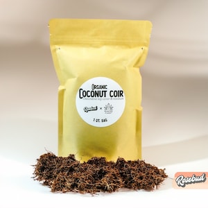 May include: A brown paper bag with a white label that reads "ORGANIC COCONUT COIR Decorative top cover & medium Rosebud x PLANTED PLANET 1 QT. BAG". The bag is sitting on a pile of brown coconut coir.