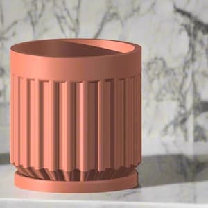 May include: A coral-colored cylindrical planter with vertical ribbed detailing. The planter sits on a matching base and is designed for indoor or outdoor use. A small potted plant is visible to the left.