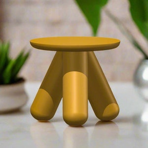 Peut inclure: Un petit tabouret à trois pieds en bois. Le tabouret est peint en jaune doré et a un dessus rond.