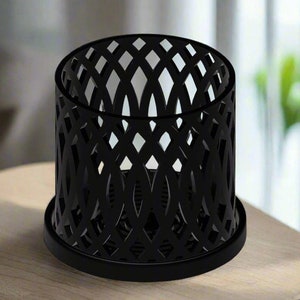 May include: Black metal candle holder with a geometric design. The holder has a round base and a cylindrical shape.