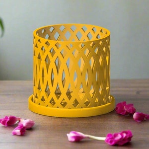 May include: A yellow metal candle holder with a geometric design. The holder has a round base and a cylindrical shape.