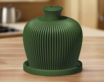 May include: A dark green ceramic diffuser with a ribbed design and a round base. The diffuser is sitting on a wooden surface.