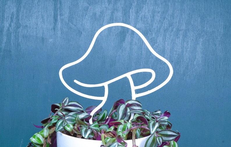 Peut inclure: Un support de plante en m&eacute;tal blanc en forme de champignon avec une plante verte et violette poussant dans un pot blanc.