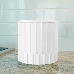 Può includere: Portaposate in ceramica bianca con un design scanalato. Il portaposate è cilindrico e ha una finitura liscia e opaca.