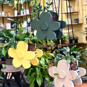 May include: Three hanging plant pots shaped like flowers. The pots are made of wood and painted in different colors: green, yellow, and beige. The pots are hanging from the ceiling by strings.