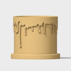 May include: A tan-colored ceramic planter with a drip design around the top edge. The planter has a wide base and a cylindrical shape.